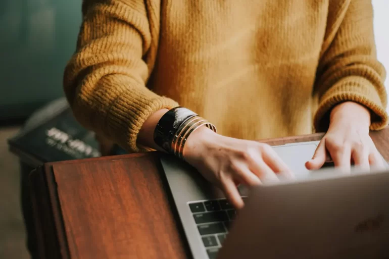 Person using a laptop computer on a desk with a notepad, pen, and smartphone nearby